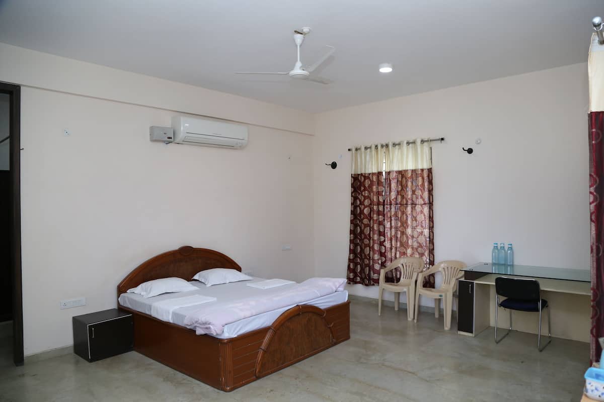 A bedroom with a bed, a desk, two chairs, an air conditioner, and a ceiling fan.