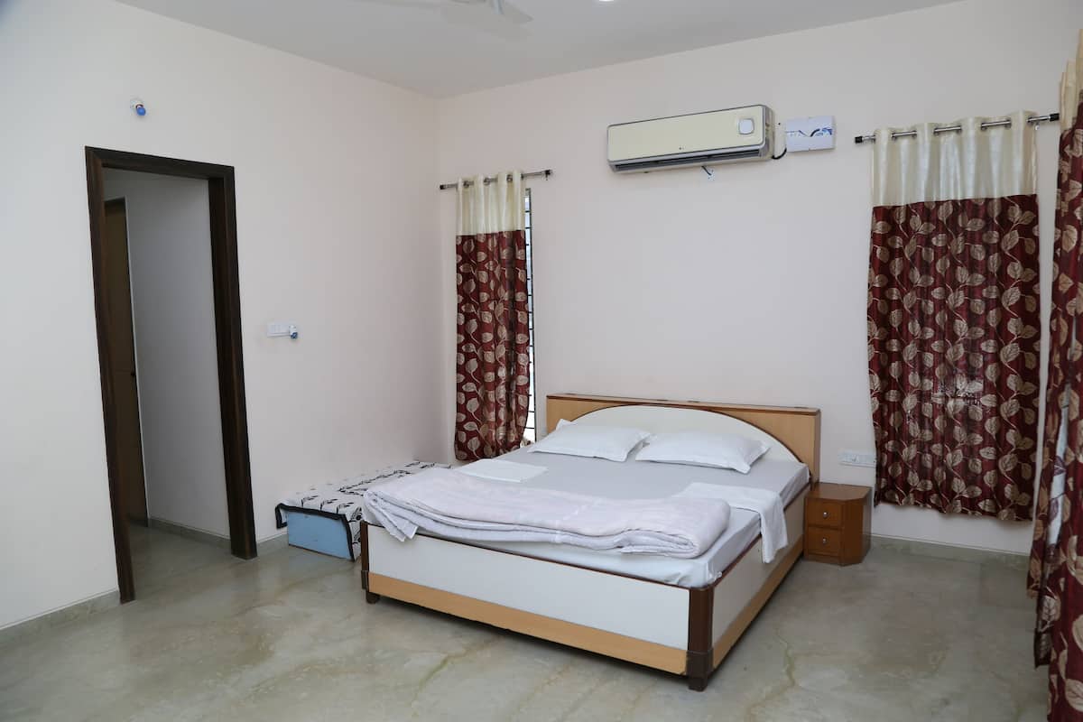 A bedroom with a bed, a nightstand, an air conditioning unit, and curtains.