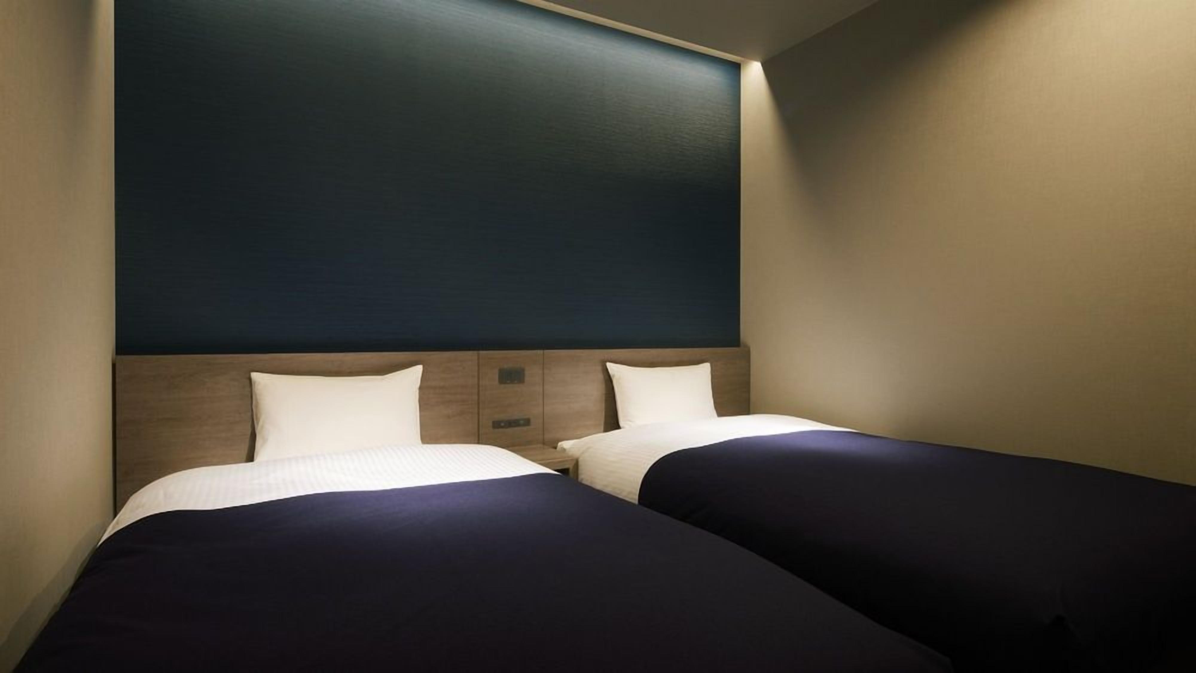 A hotel room with two beds, a dark headboard, and a light-colored wall.