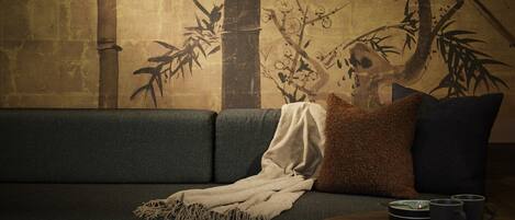 A room with a sofa against a wall featuring a bamboo and branch painting.
