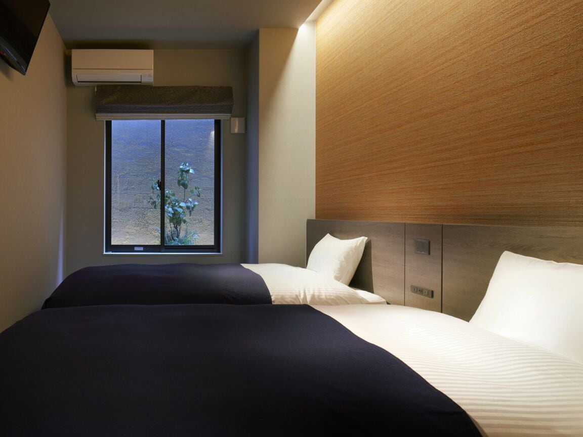 A modern hotel room with a large bed, a window with a view of a desert landscape, and a wooden headboard.