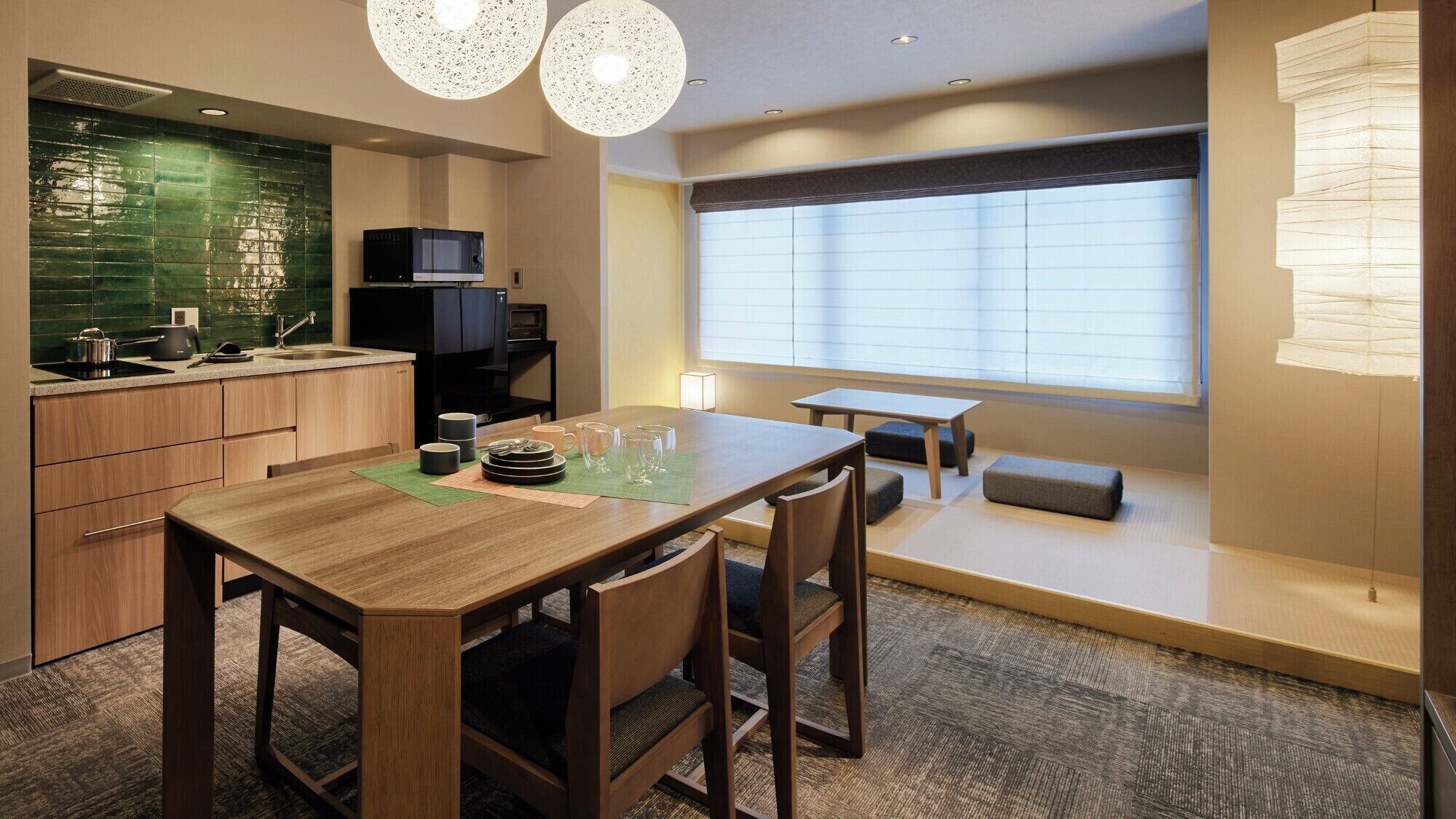 Habitación de hotel compacta con comedor, kitchenette y un amplio ventanal que proporciona luz natural.