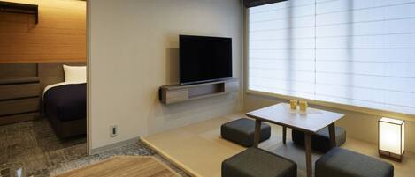 Habitación de hotel moderna con cama, televisión de pantalla plana, pequeña mesa de comedor y ventana grande.