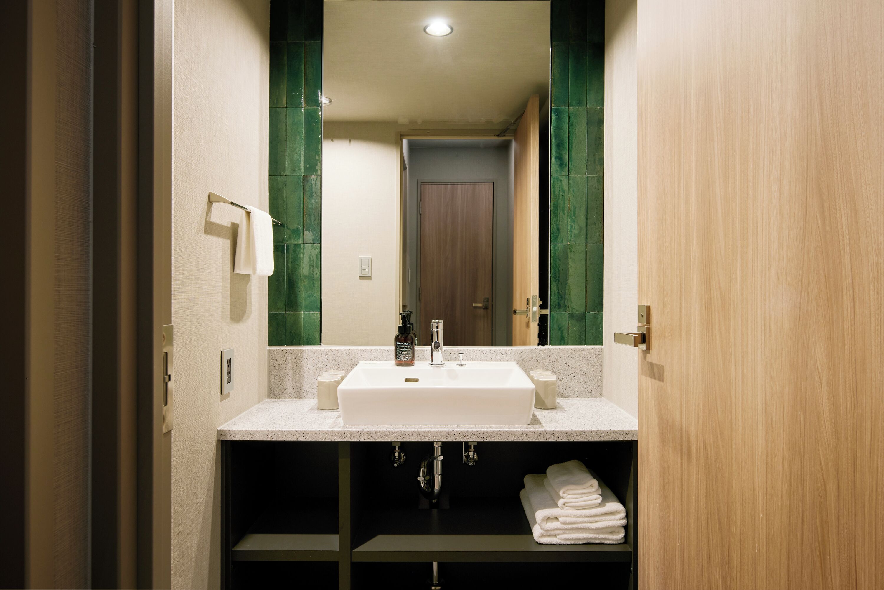 A modern bathroom with a large mirror, white sink, and green-tiled walls.