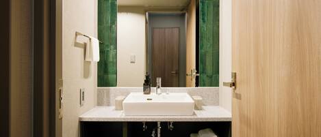 A modern bathroom with a large mirror, white sink, and green-tiled walls.