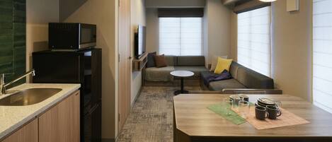 Una cocina compacta con microondas y refrigerador, un comedor con mesa y sillas, y una sala de estar con sofá y cojines.