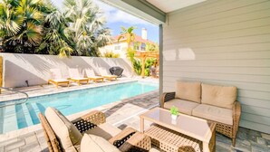 A poolside area with lounge chairs, a sofa, and a table. - Another Day In Paradise - Coastal Holiday! (St. Augustine Vilano Beach)