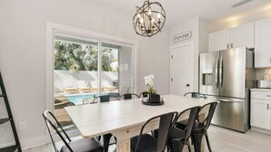 A modern kitchen with a stainless steel refrigerator, white cabinets, and a dining area with a white table and black chairs. - Another Day In Paradise - Coastal Holiday! (St. Augustine Vilano Beach)
