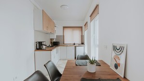 A modern kitchen with white cabinets, a wooden countertop, and a dining area with a wooden table and chairs. - THE NOOK APARTHOTEL  (Timisoara)