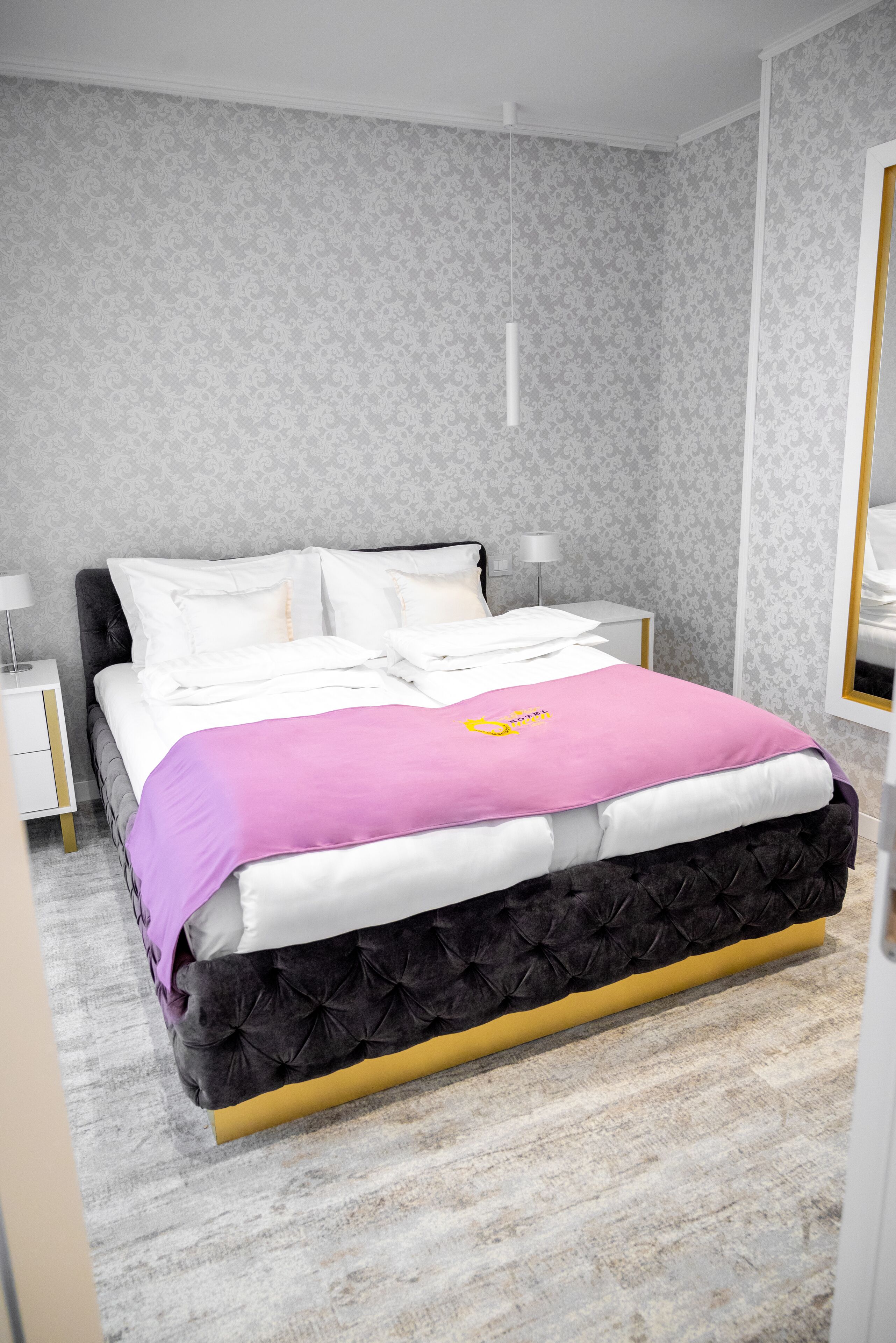 Un dormitorio con cama, mesitas de noche, lámpara y espejo.