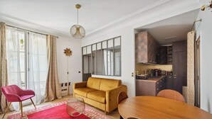 A modern living room with a sofa, a dining table, and a kitchen area visible through an open door. - Etoile Apartment (G1) – Luxury Two-Bedroom (Paris)
