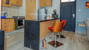 A compact kitchen with wooden cabinets, a black countertop, and a coffee machine. - 4 minutes to Two Rivers Mall! Family-sized condo with a fully functional Kitchen (Ruaka)