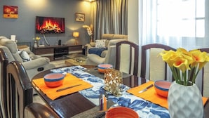 A living room with a fireplace, a TV, and a dining area with a table set for two. - 4 minutes to Two Rivers Mall! Family-sized condo with a fully functional Kitchen (Ruaka)