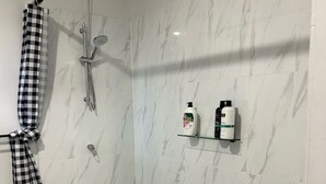 A shower with a checkered towel, a glass shelf with toiletries, and a marble wall. - Clermont Guest House (Clermont)