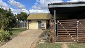 A building with a metal roof and a number '3' sign, a gravel driveway, and a grassy area with a fence. - Clermont Guest House (Clermont)