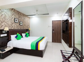 Une chambre d’hôtel équipée d’un lit, d’une télévision, d’un bureau, d’une lampe et d’un mur orné d’un motif décoratif.