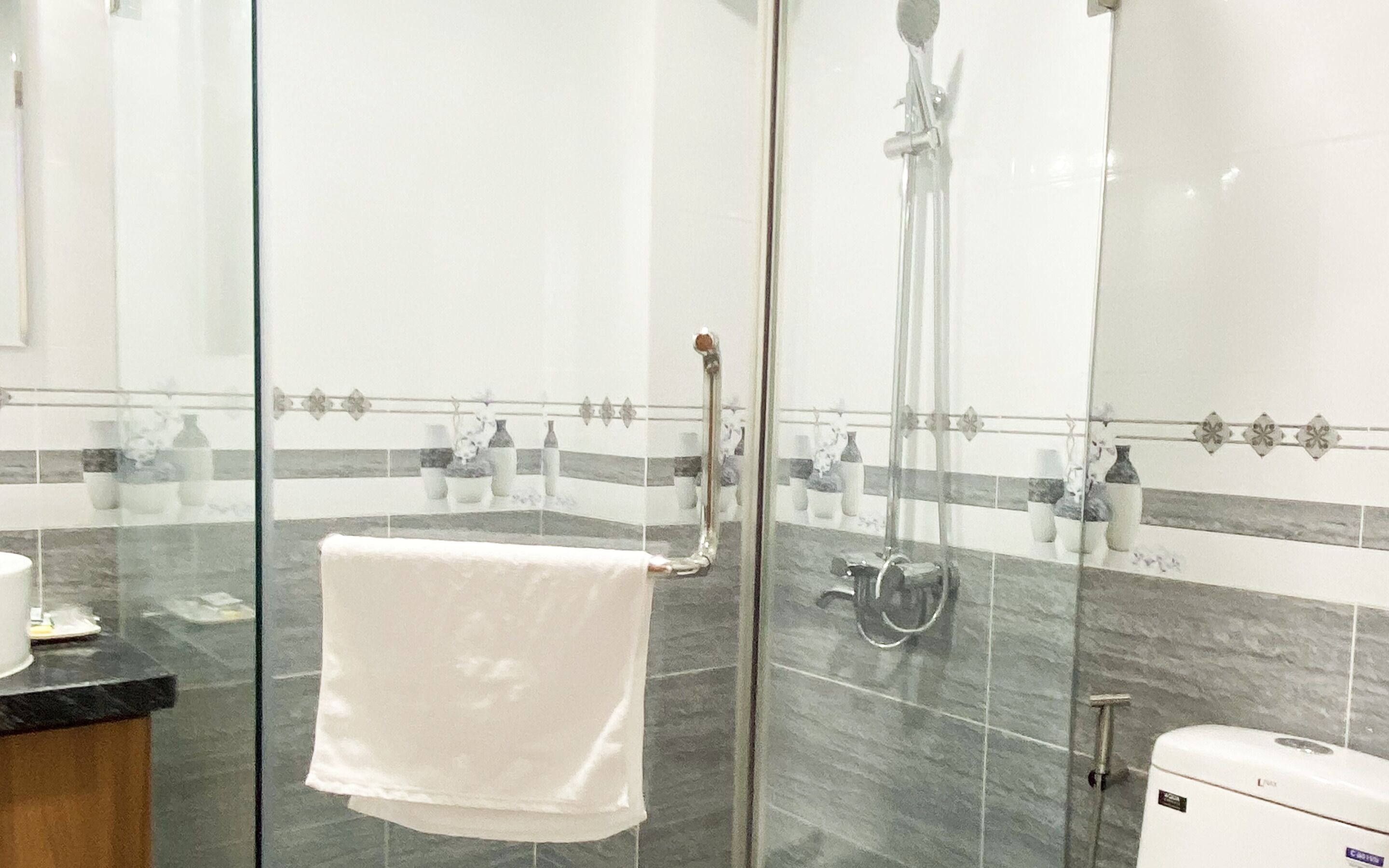 Ein modernes Badezimmer mit einer Duschkabine aus Glas, einem weißen Handtuch auf einem Halter und einer Toilette mit sichtbarem Markenlogo.