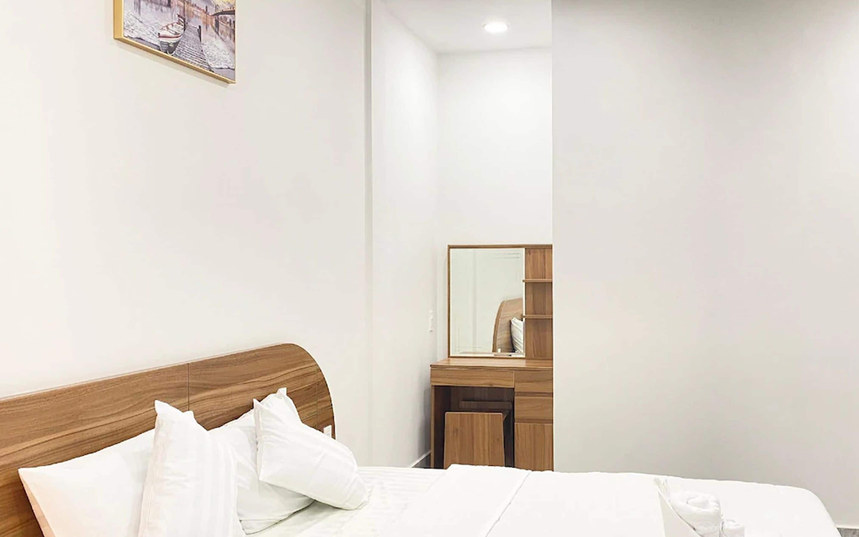 A neatly made bed with white linens and pillows, a wooden headboard, a bedside table with a mirror, and a framed picture on the wall.