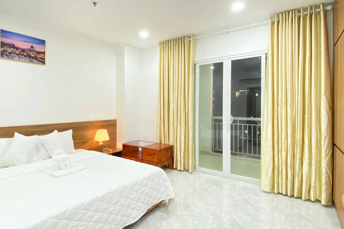A hotel room with a bed, a nightstand, a lamp, a painting, and a sliding glass door to a balcony.
