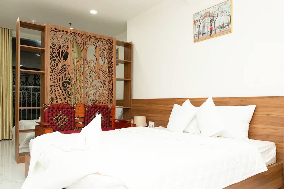 A hotel room with a large bed, a decorative wooden partition, a wooden headboard, and a painting on the wall.