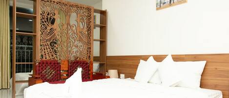 A hotel room with a large bed, a decorative wooden partition, a wooden headboard, and a painting on the wall.