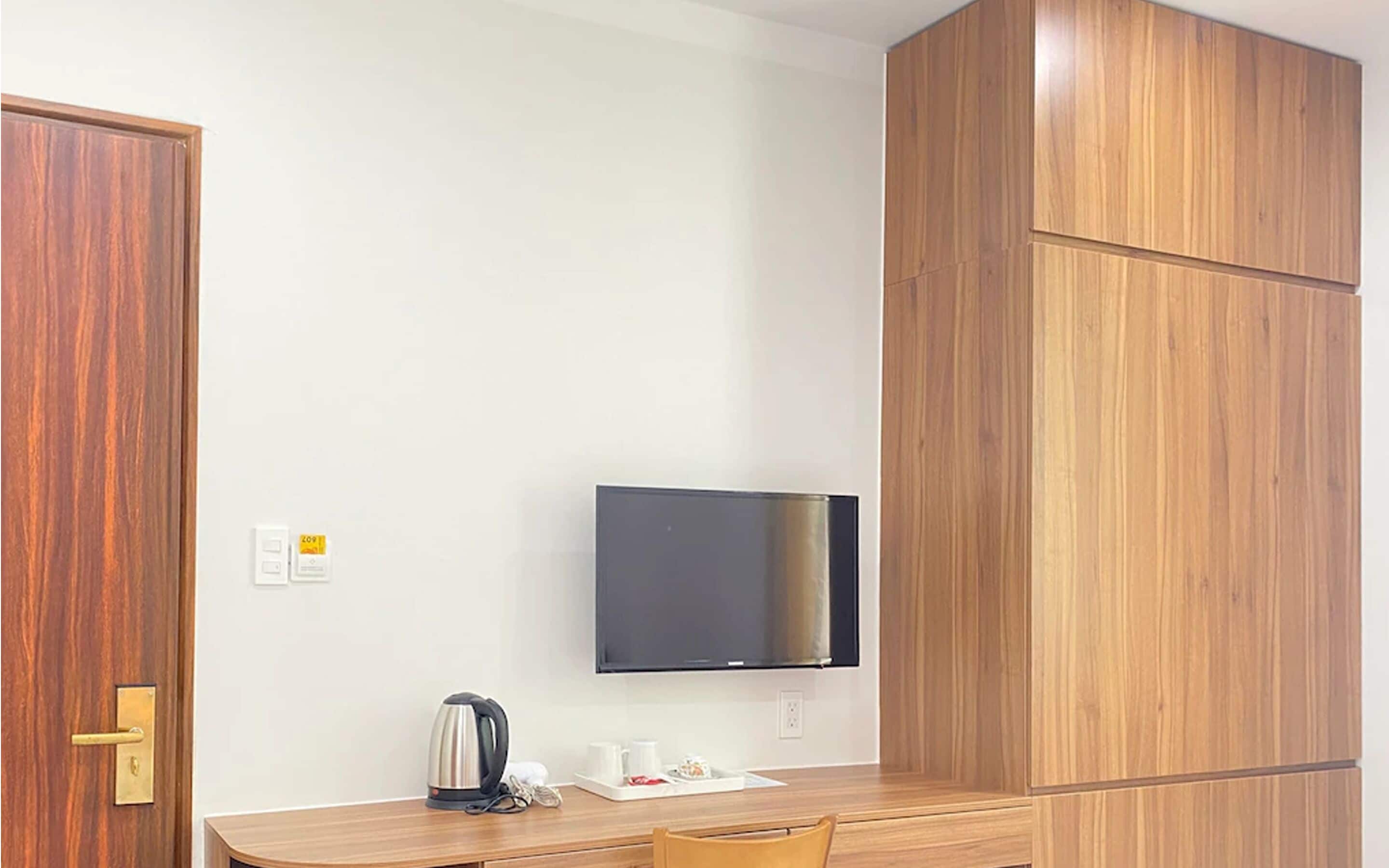 A hotel room with a wooden desk, a television mounted on the wall, and a door with a brass handle.