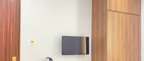 A hotel room with a wooden desk, a television mounted on the wall, and a door with a brass handle.