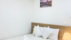 Hotelkamer met een bed, witte kussens, een houten hoofdbord, een wandairconditioner en een lijst met een stadsgezicht.