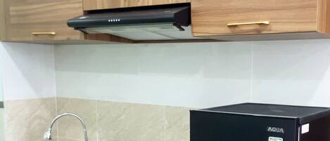 A kitchen with wooden cabinets, a stainless steel sink, a black range hood, and a black refrigerator.