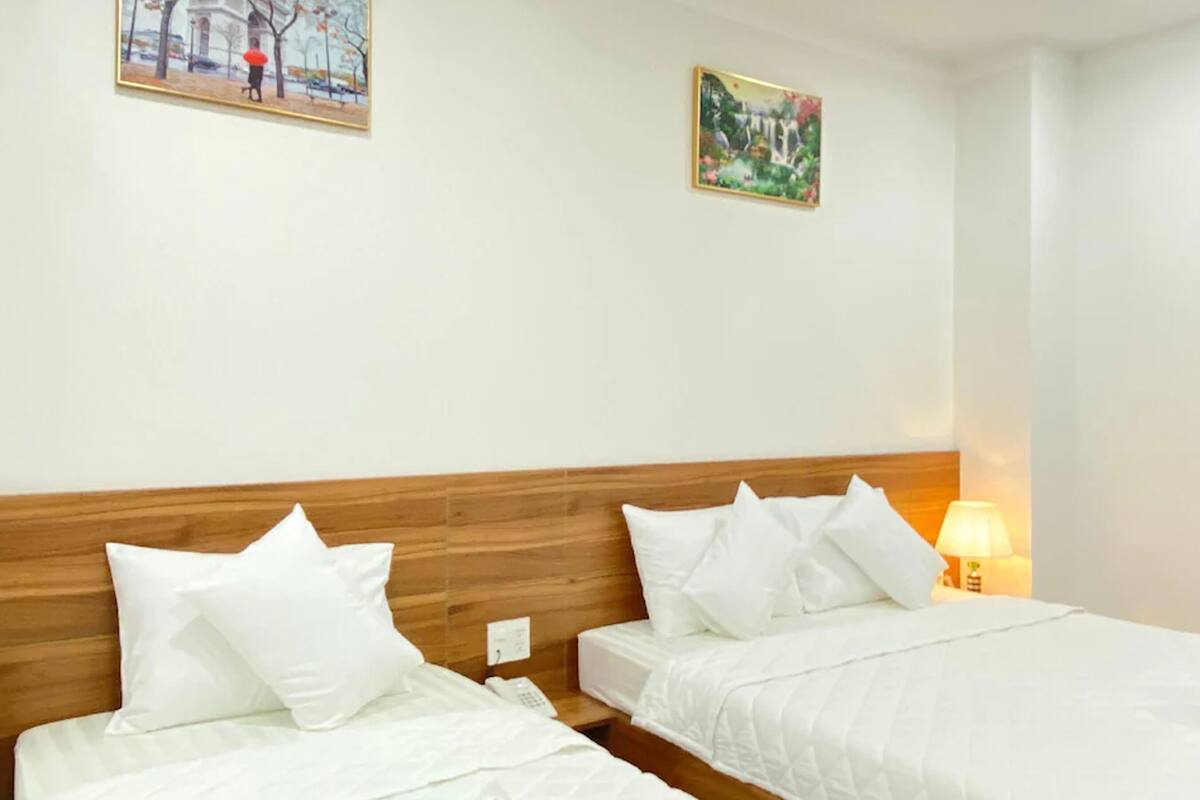 A hotel room with two beds, wooden headboards, white bedding, a bedside lamp, and two framed pictures on the wall.