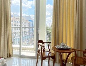 A room with a large window, a wooden chair, a small table with a tray, and curtains. - Thiên Tài Hotel (Ho Chi Minh City)