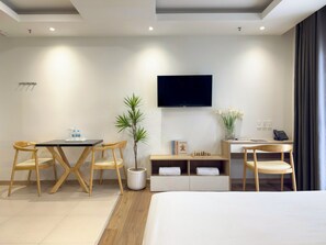 Una habitación de hotel moderna con una cama, un escritorio con una silla, un televisor, una planta y una pequeña estantería.