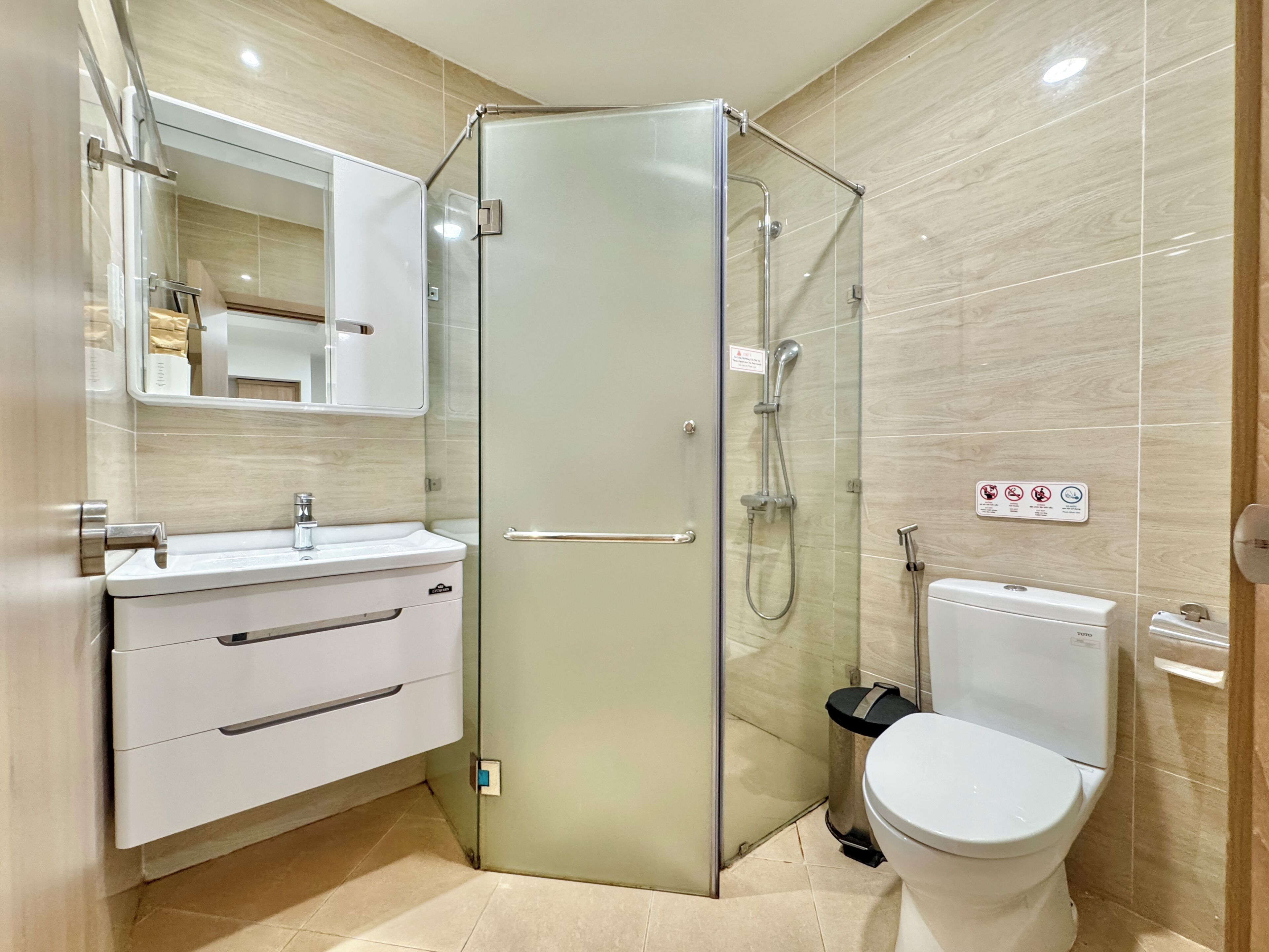 Een moderne badkamer met een douchecabine van glas, een wit wastafelmeubel met spiegel en een toilet.