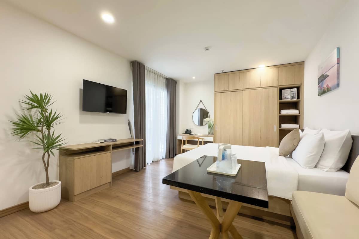 Ein modernes Hotelzimmer mit Flachbildfernseher, einem Holztisch, einem Bett mit weißer Bettwäsche, einem Couchtisch und einer Topfpflanze.