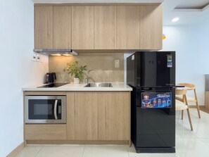 Une cuisine moderne avec des meubles en bois, un four encastré, un évier, un réfrigérateur noir et une petite plante en pot.