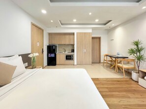 A modern hotel room with a bed, a small kitchenette, a dining area, and a potted plant. - CityHouse NEST LightHouse Saigon (Ho Chi Minh City)