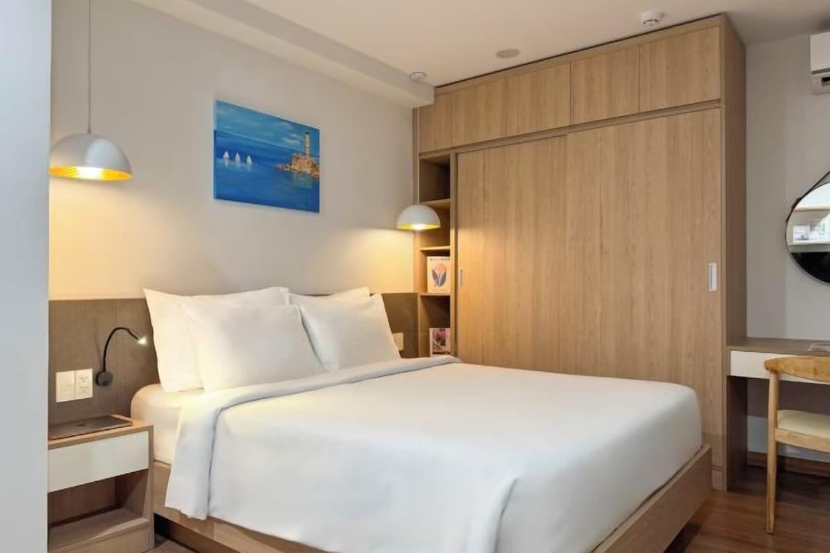 Una cama bien hecha con ropa de cama blanca, un armario de madera y un escritorio con una silla.