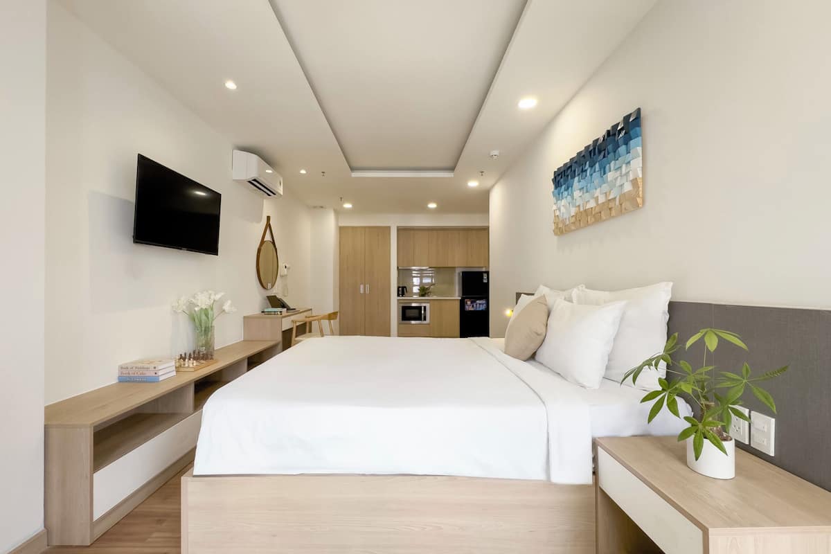 Ein modernes Hotelzimmer mit einem großen Bett, einem Fernseher, einem Schreibtisch und einer kleinen Küchenzeile im Hintergrund.