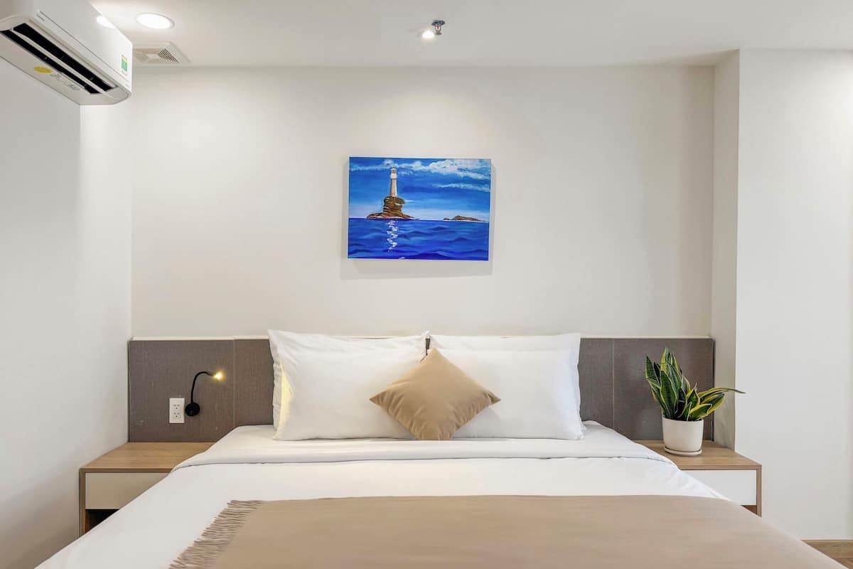 Ein Hotelzimmer mit einem Bett, einem Leuchtturm-Gemälde, einer Topfpflanze und einer Klimaanlage.