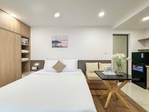 Una habitación de hotel con cama, una mesita, un refrigerador y un cuadro en la pared.