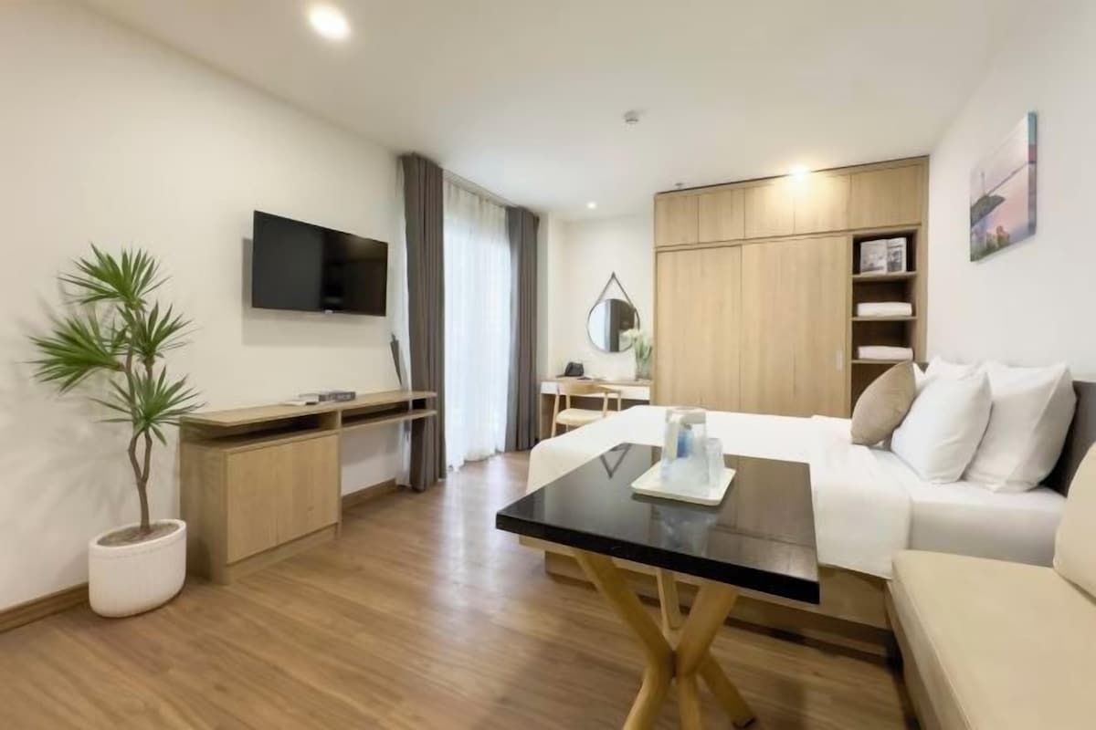 Una habitación de hotel moderna con una cama, un escritorio, un televisor, una planta y un armario.