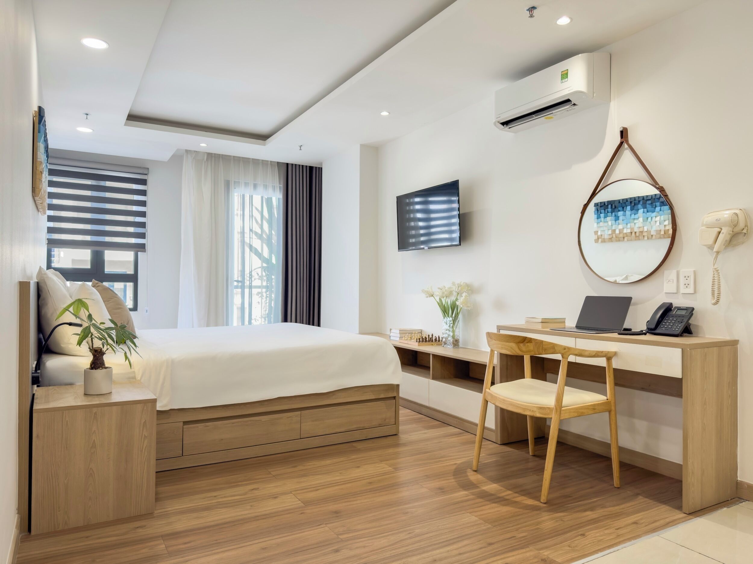Habitación de hotel con cama, escritorio, silla, televisor, aire acondicionado y espejo.