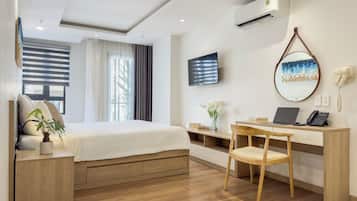 Habitación de hotel con cama, escritorio, silla, televisor, aire acondicionado y espejo.