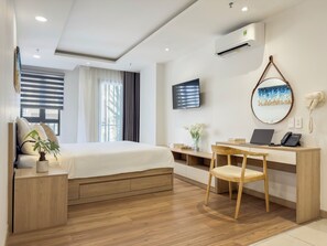 A hotel room with a bed, desk, chair, TV, air conditioning unit, and a mirror.