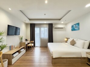Habitación de hotel con cama, escritorio, silla, televisor, equipo de aire acondicionado y un cuadro en la pared.