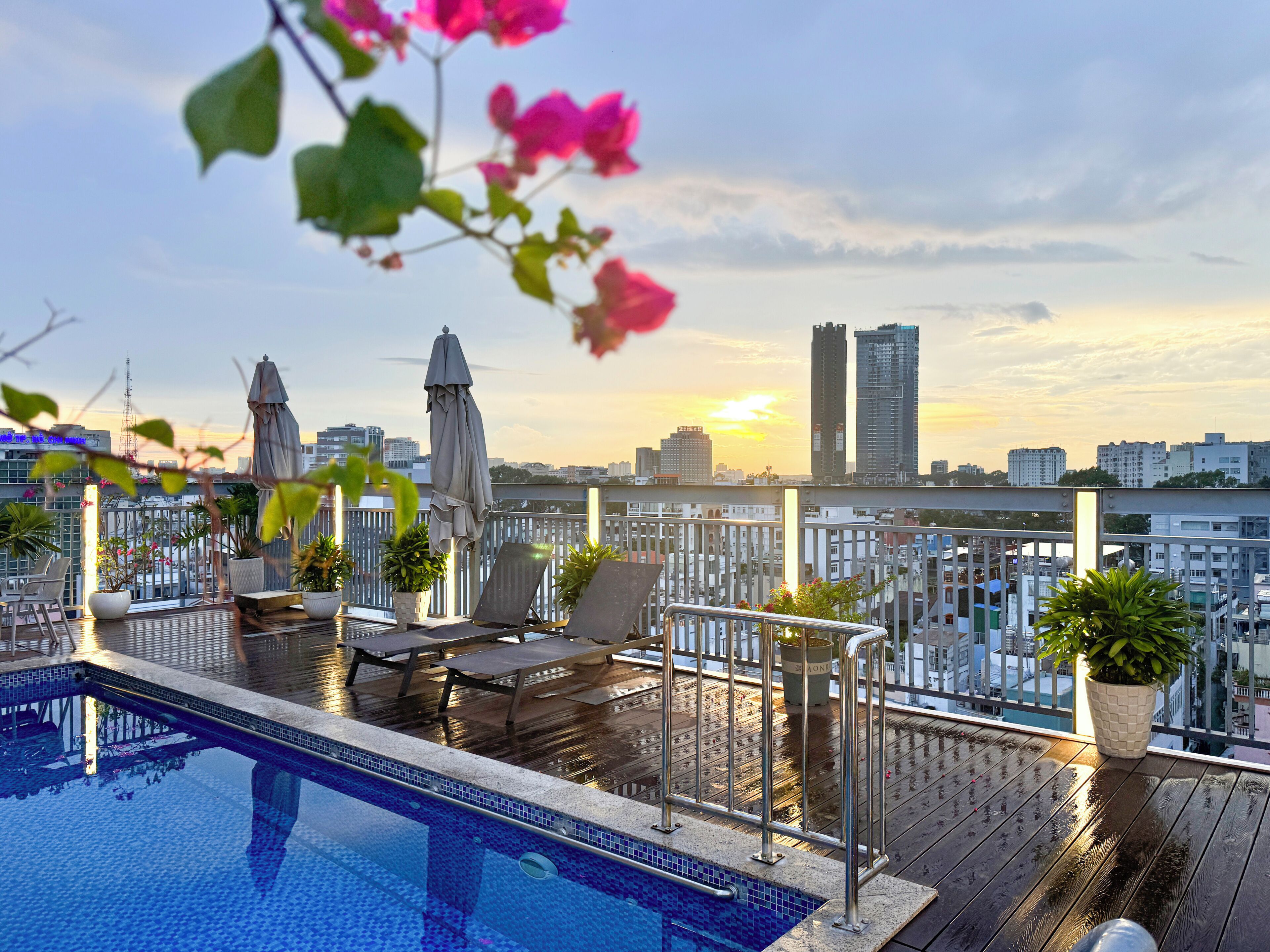 A rooftop pool with lounge chairs and umbrellas, overlooking a cityscape with tall buildings.