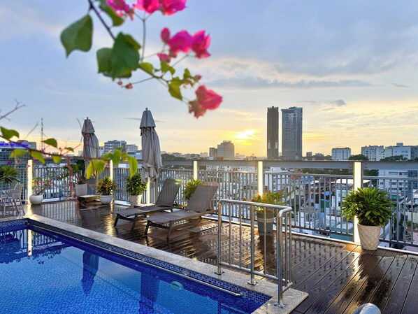 Una piscina en la azotea con sillas de descanso y sombrillas, con vistas a un paisaje urbano de edificios altos.