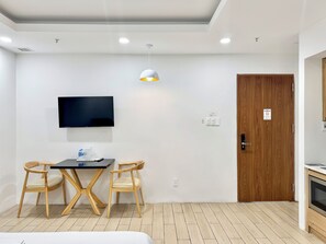 A room with a TV mounted on the wall, a wooden door, a table with two chairs, and a pendant light.