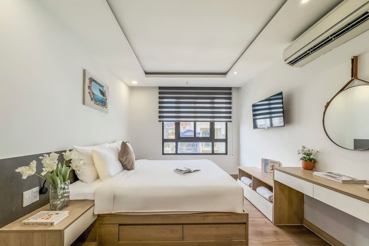 Ein modernes Hotelzimmer mit Bett, Nachttisch, Fernseher und einem Fenster mit Jalousien.