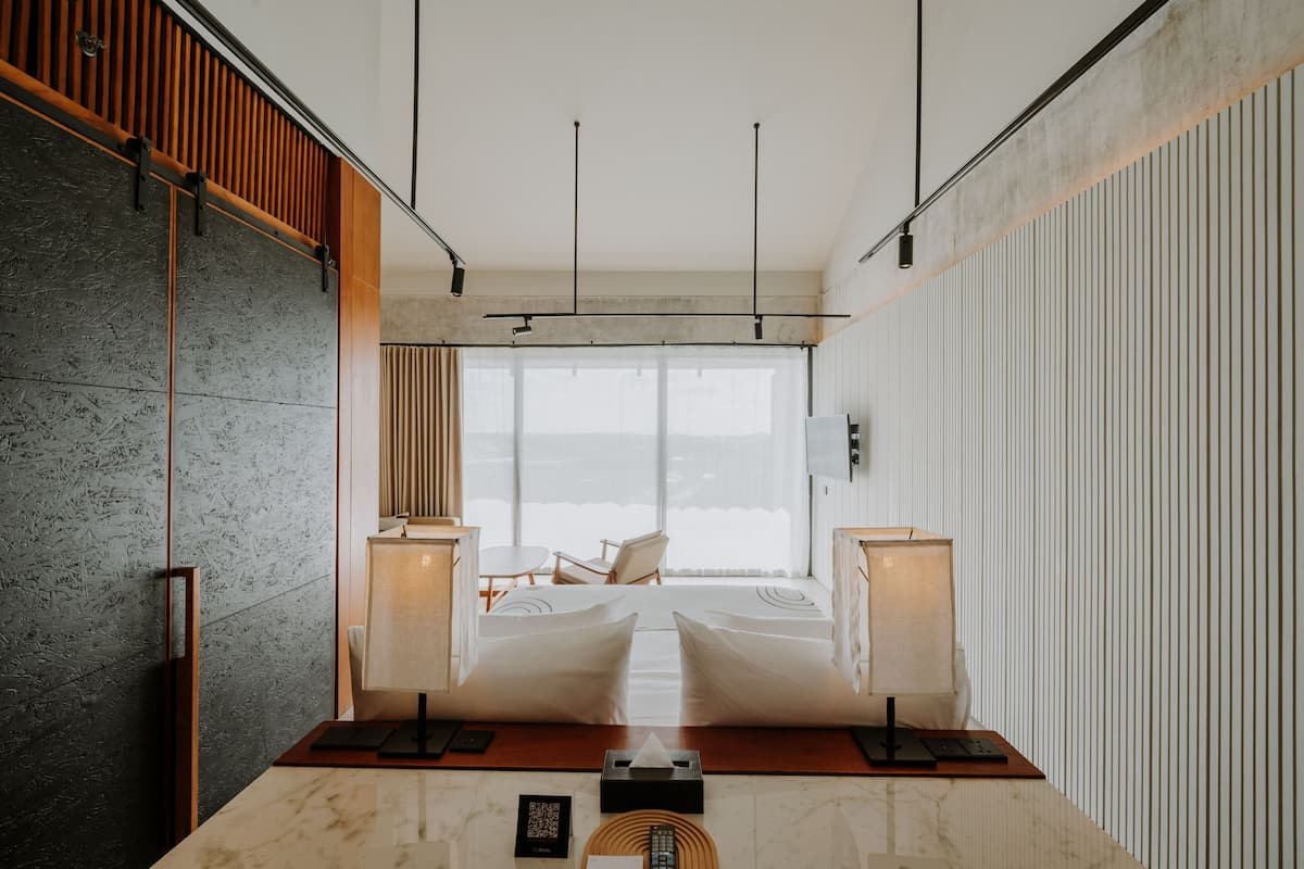 Una habitación de hotel moderna con un ventanal grande, un panel de pared de listones de madera, una mesa con cubierta de mármol y una lámpara de noche.